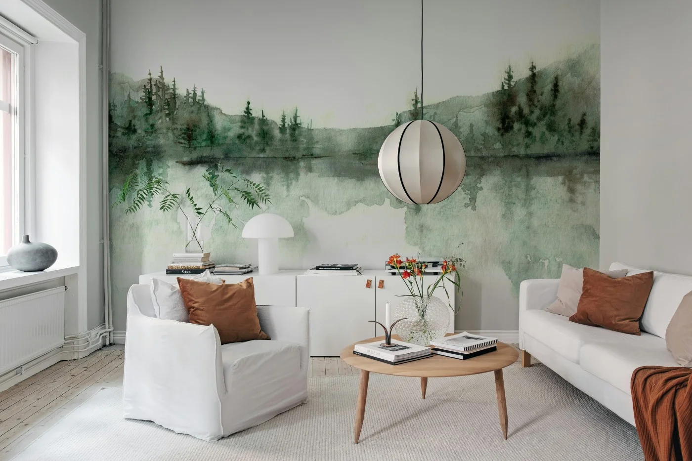 Living room with a soft watercolour forest and lake mural covering the wall behind a pale sofa